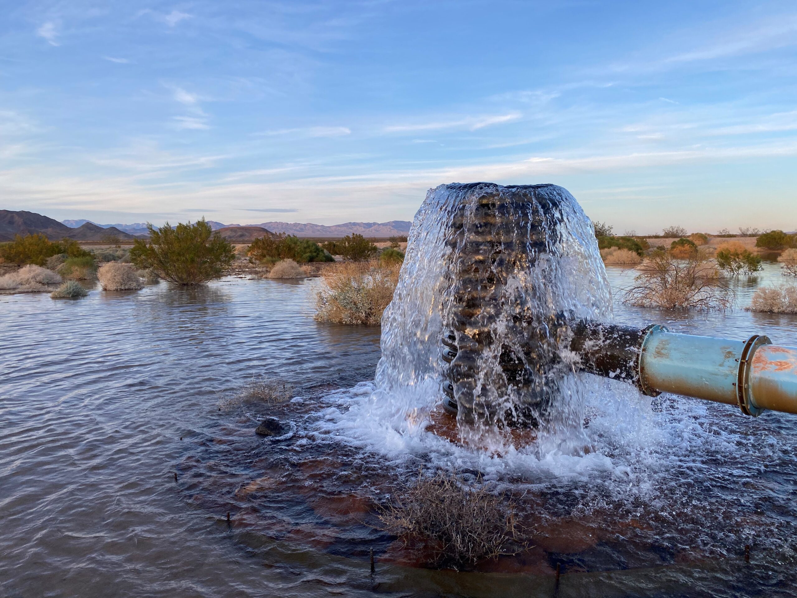 Water gushes from a pipe and spills down over the sides like a fountain to fill a groundwater recharge basin an an arid environment.